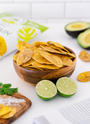 Bowl of Artisan Tropic Sea Salt Plantain Strips With Limes and Avocados in the foreground and background