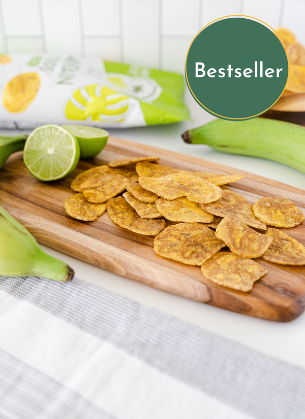 Bestseller Cutting board with Artisan Tropic's Sea Salt Plantain Strips, limes and green plantains in the background