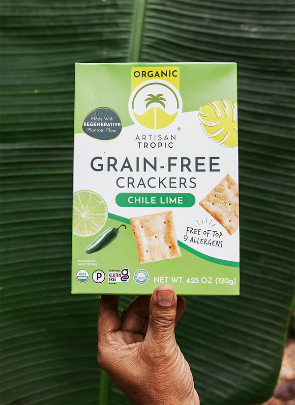 Artisan Tropic Chile Lime Crackers held by a farmer's hand over a plantain leaf