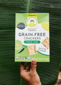 Artisan Tropic Chile Lime Crackers held by a farmer's hand over a plantain leaf