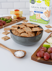 Artisan Tropic Sea Salt Crackers in a bowl by a board with olives, grapes, and sliced pears