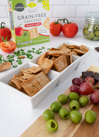 Artisan Tropic Tomato Herb Crackers in a white bowl by a board with olives and grapes