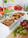 Artisan Tropic Tomato Herb Crackers in a white bowl by a board with olives and grapes